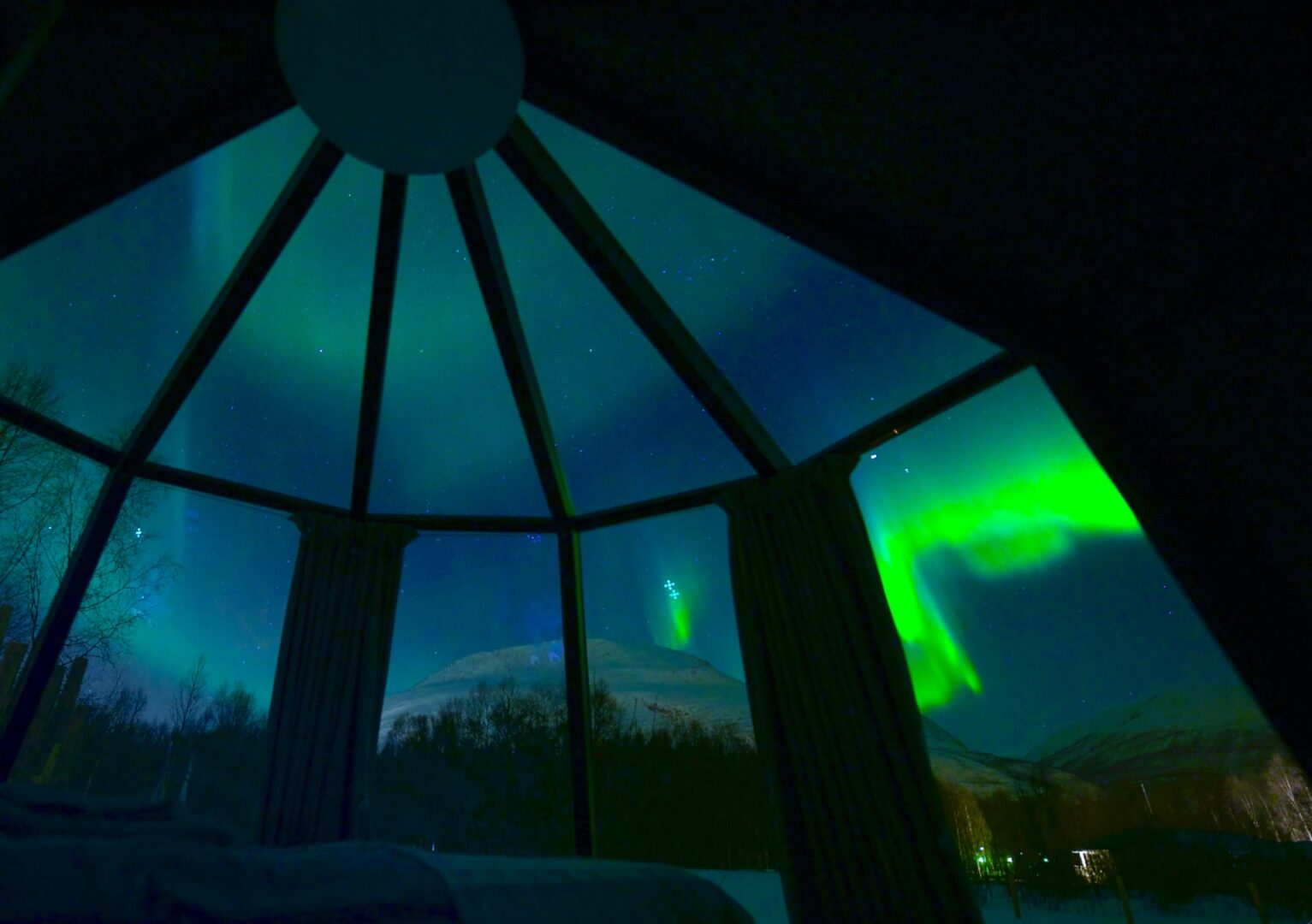 Northern lights seen through the glass roof of an AuroraHut
