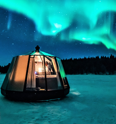 AuroraHut glass igloo glowing under the northern lights