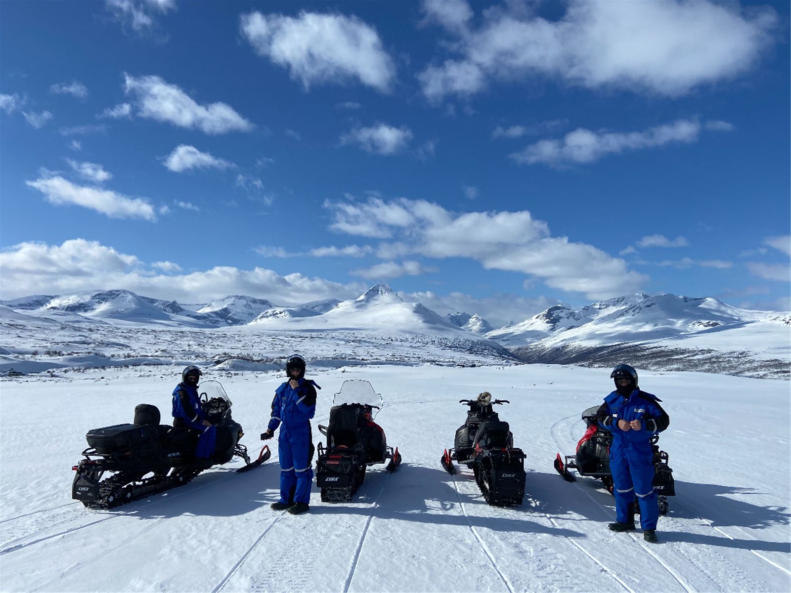 Guests standing beside snowmobiles in a sunny Arctic landscape